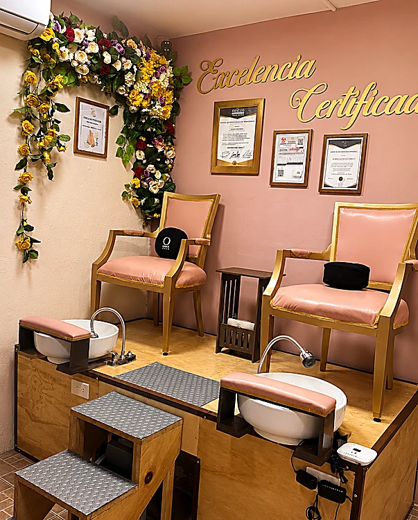 Estación de pedicure con dos sillones rosa, tinas sobre escalones de madera y guirnalda de flores junto al rótulo dorado