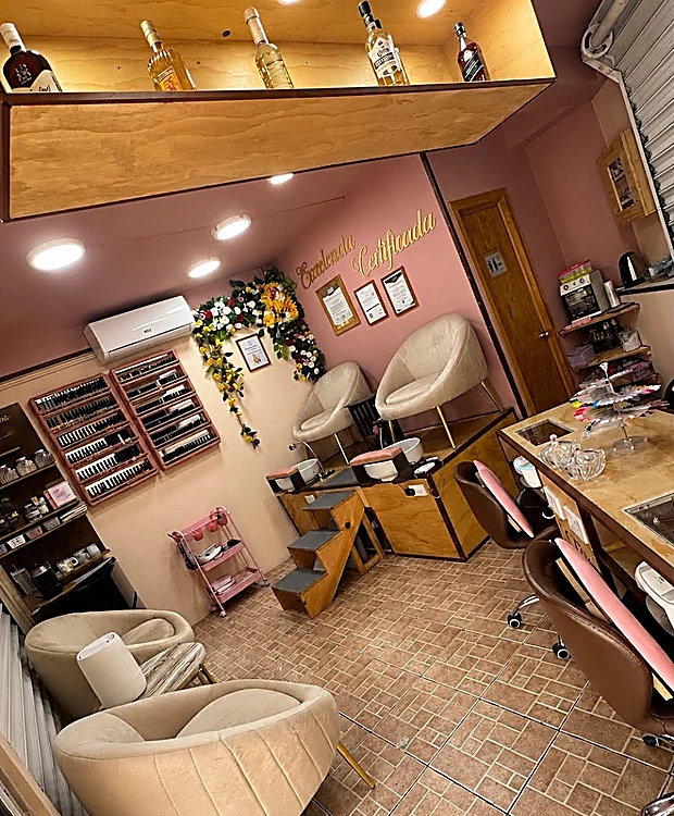 Vista del salón desde la entrada: muro rosa, repisa dorada iluminada, sillones color crema y mueble de esmaltes