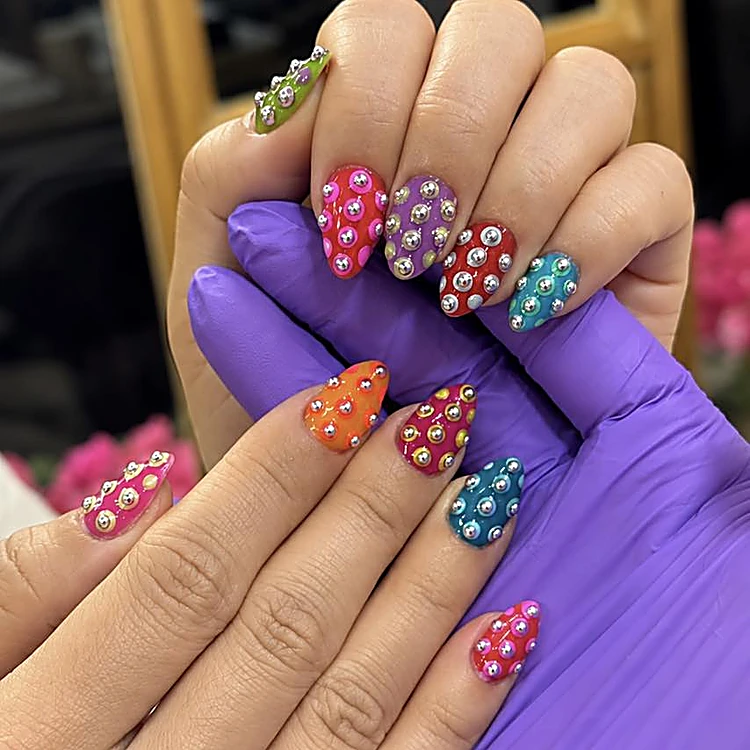 Uñas en colores vivos cubiertas de piedras plateadas