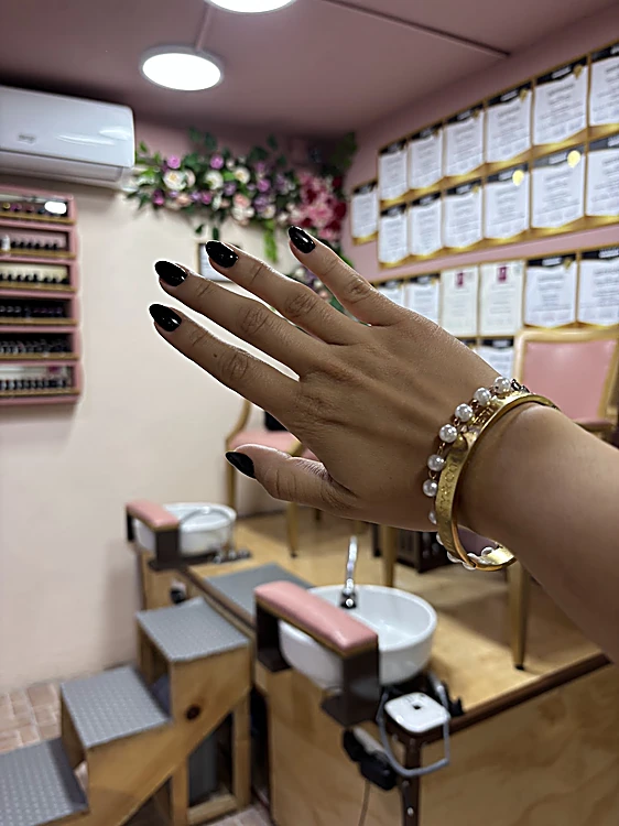 Mano con uñas almendra negras frente a la estación de pedicure y la pared de certificados