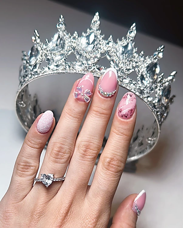 Uñas rosa con piedras y brillos, con una corona de cristal detrás